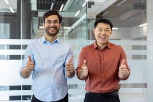 Two smiling men in an office setting, expressing positivity with thumbs up gestures, symbolizing success and teamwork. The image conveys a friendly and professional atmosphere photo