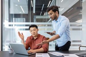 In a modern office, two colleagues are engaged in a discussion. One holds a smartphone while the other uses a laptop. The scene captures the essence of collaboration and teamwork. photo