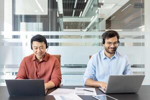 Two professionals wearing headsets are focused on their laptops in a modern office. This image captures a collaborative work environment, showcasing technology, communication, and productivity. photo