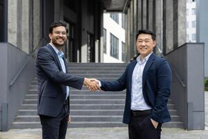 Two business professionals in formal attire exchange a confident handshake outside a modern office. The image captures a moment of agreement and partnership, symbolizing connection and success. photo