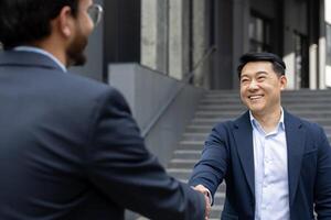 Two business professionals in formal attire shaking hands, symbolizing a successful partnership. The outdoor setting and bright smiles convey trust, connection, and collaboration. photo