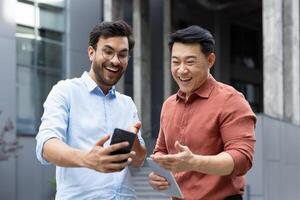 Two colleagues share a joyful moment outside, interacting with a smartphone and tablet. The scene captures a friendly, energetic vibe highlighting modern technology and communication. photo