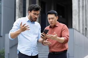 Two men appear concerned as they look at a smartphone screen, surprised and perplexed. Their expressions suggest confusion or unexpected news, engaging in conversation, likely about a tech problem. photo