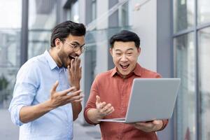 Two ecstatic colleagues celebrate a surprising success while looking at a laptop screen. Their joyous expressions and the laptop highlight a moment of achievement and teamwork. photo