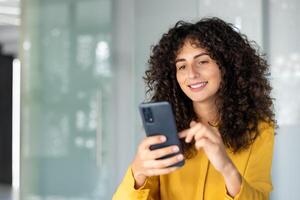 Confident woman smiles using hone for communication indoors. Displaying modern technology usage, connected and joyful. Concept of digital lifestyle. photo