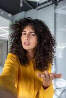 Confident woman gesturing while taking selfie with smartphone. Indoors setting adds modern and casual vibe to image. photo