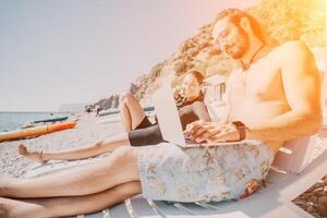 Beach Laptop Work Couple - Man and woman work on laptop while relaxing on beach chairs. photo