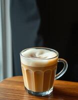 Warm coffee with frothy texture served in a glass on a wooden table by the window in a cozy cafe atmosphere photo