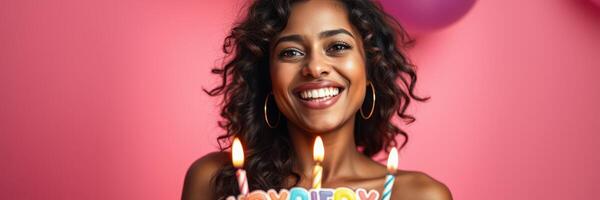 Woman celebrates her birthday with a joyful smile, holding a cake with candles against a colorful backdrop photo