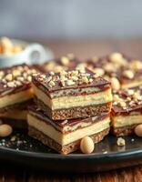 Decadent layered dessert squares with chocolate, peanut butter, and crunchy toppings displayed on a black plate photo