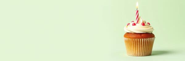 Colorful cupcake with white frosting and a candle stands on a green background for a birthday celebration photo