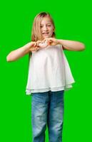 Young girl in a white top joyfully making a heart shape with her hands against green background photo