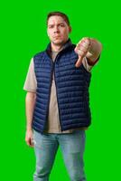 Man in a blue vest showing a thumbs down gesture with a bright green background photo