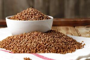 Bowl of raw uncooked buckwheat on wooden table photo
