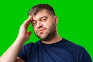 A man with closed eyes holds his head in a thoughtful pose against a bright green backdrop photo