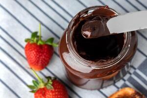 Top view of knife in chocolate paste with strawberries on white napkin photo