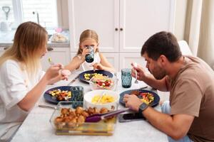 A family enjoys a meal together in their kitchen, with the young girl taking a drink photo