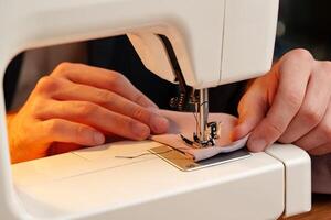 Hands sewing fabric using a sewing machine on a wooden table in a well-lit workspace photo