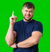 A man with a friendly smile gestures upwards while wearing a navy shirt against a bright green background photo