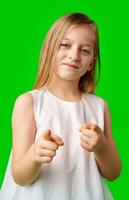 A young girl in a white dress playfully poses with a smile and finger guns against a vibrant green background photo