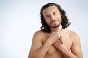 A man with curly hair grooming his beard in a well-lit space while using a straight razor photo