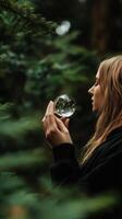 Woman holds crystal ball in serene forest setting, contemplating nature and reflections during tranquil moment photo