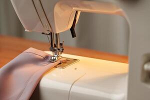 Sewing machine in use on a wooden table, stitching a light fabric in a well-lit indoor workspace photo