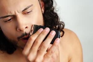 Man trimming his beard indoors using an electric trimmer while showcasing his personal grooming routine photo
