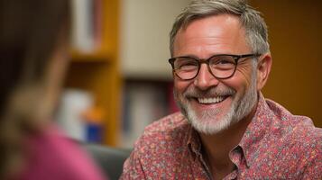 A cheerful man wearing glasses smiles while having a conversation in a cozy environment photo