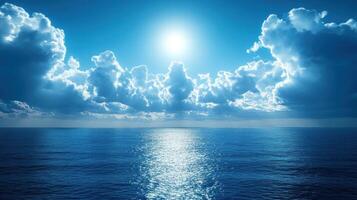 Bright sunlight glistens on calm ocean waters with soft clouds in a clear blue sky photo