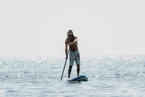 Man Paddleboarding Ocean Water Sport - A man paddleboards on a calm ocean on a sunny day. photo
