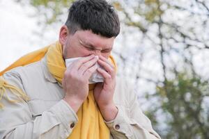 young man enjoying autumn days breathing fresh air using tissue to wipe nose photo