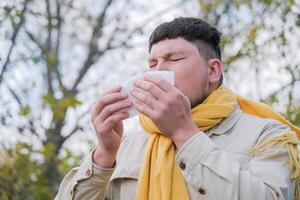young man enjoying autumn days breathing fresh air using tissue to wipe nose photo
