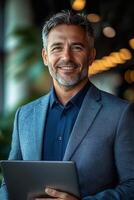 A young businessman smiling confidently while holding a laptop in a sleek urban environment. photo