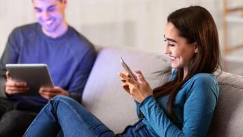Modern Technologies Concept. Beautiful spouses sitting on couch in their apartment, using digital tablet and smart phone photo