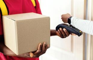 Cropped Shot Of Customer Lady Paying Courier For Parcel Delivery Using Smartwatch, Putting Watch To Payment Terminal At Home. Selective Focus On Cardboard Box photo