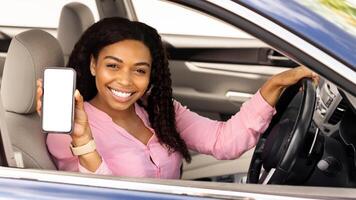 Happy black female driver holding smartphone with blank screen in hand, mock up, lady showing cell phone with white empty display, using mobile app for navigation, riding in city, free copy space photo
