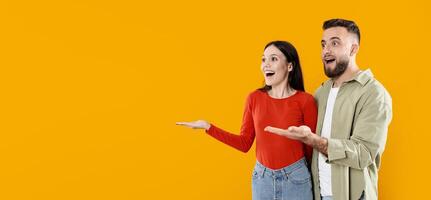 A young couple dressed casually expresses joy and excitement, looking surprised while gesturing with their hands at copy space. Their bright background adds to the cheerful atmosphere. photo