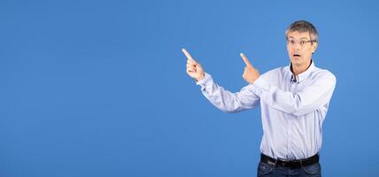 A middle aged Caucasian man in his 50s expresses excitement and engagement, pointing with both hands at copy space photo