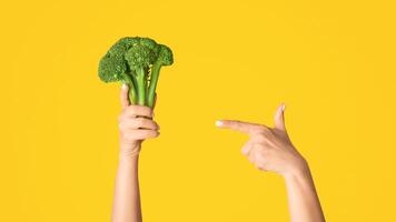 Woman pointing at broccoli in her hand against pink background, close up view. Panorama photo