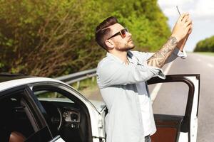 Unhappy Caucasian man standing near car, having problem with mobile connection, trying to find network on highway. Road emergencies, no signal, calling breakdown service concept photo