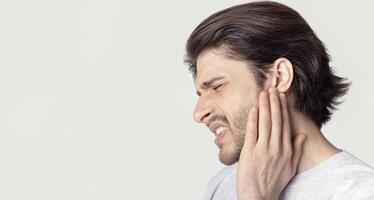 Man with ache holding ear isolated on gray background photo