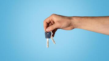Unrecognizable young guy showing keys to new home on blue background, closeup. Copy space. Panorama photo