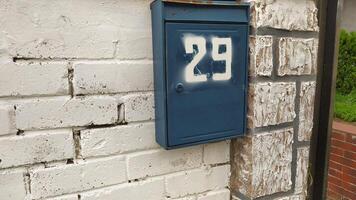 A charming blue mailbox featuring the number 29 beautifully affixed to a classic brick wall photo