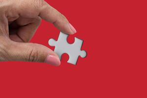 Hand holding a jigsaw piece with copy space isolated on red background. Concept of missing and key success photo