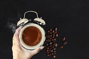 coffee beans and hand with alarm clock on black background photo