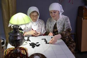 Mother and daughter in traditional village festive clothes play a board game of dominoes. The concept of a joint holiday, family traditions, dementia prevention photo