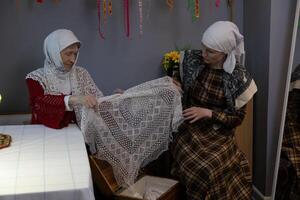 Two women in traditional clothing are working on a lace pattern photo