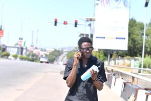 A man is talking on his cell phone while walking down the street. He is wearing a black shirt photo