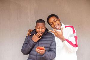 two young african men standing outside excited and delighted while using there smart phone photo